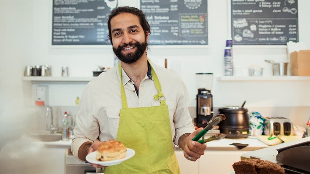 Cafe worker behind counter with a cake and cooking tongs